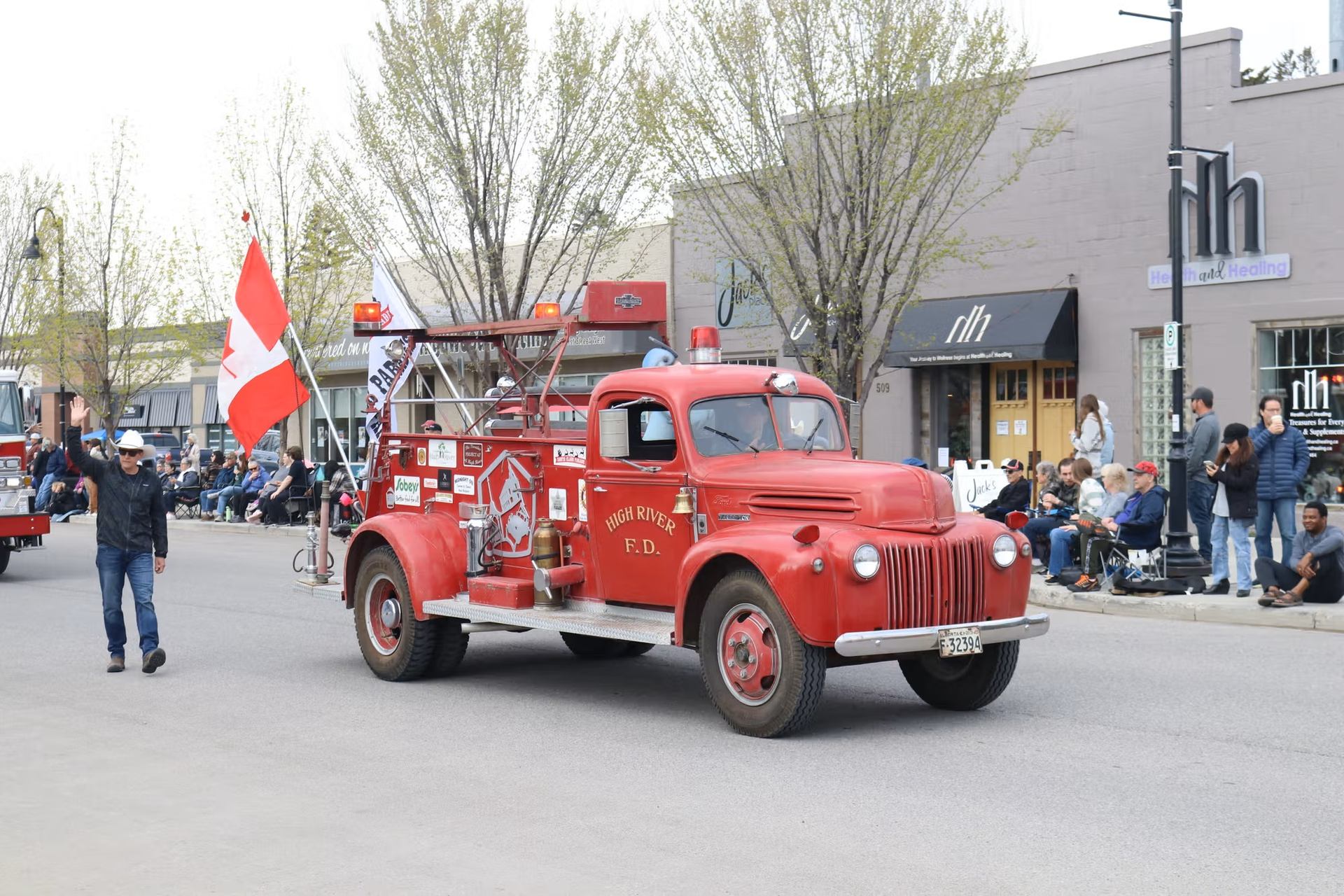 Vintage High River fire truck drives in parade with Canadian flag and spectators.