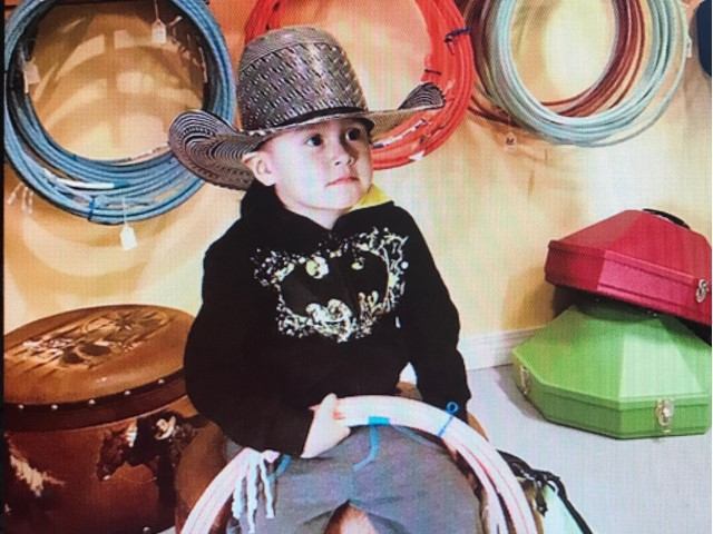 Child wearing a cowboy hat near colorful suitcases and coiled ropes inside a shop.
