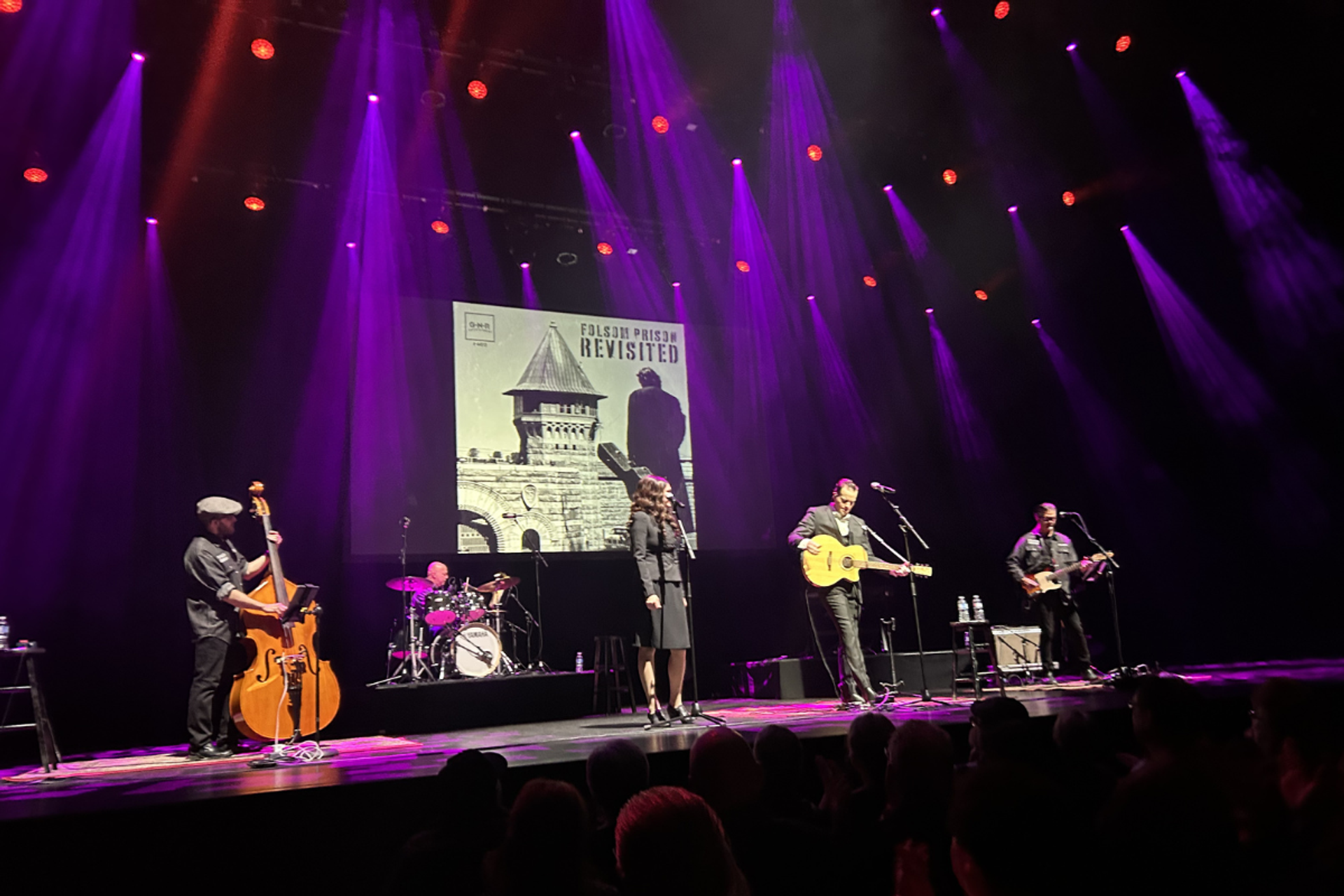 Band performs on stage under purple lights with Folsom Prison Revisited backdrop.