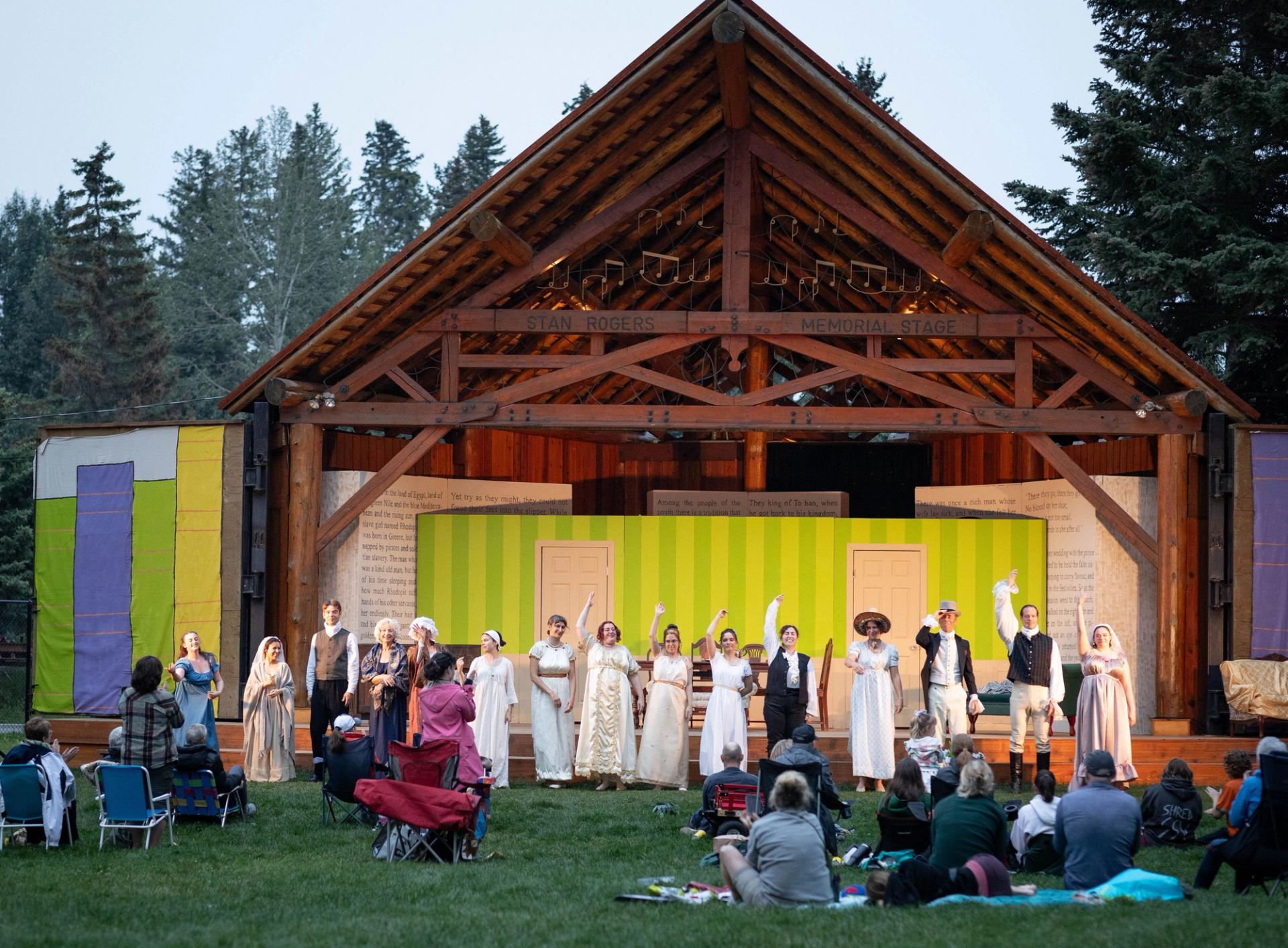 Cast in period costumes bows to an outdoor audience on the Stan Rogers Memorial Stage during a theatre performance.