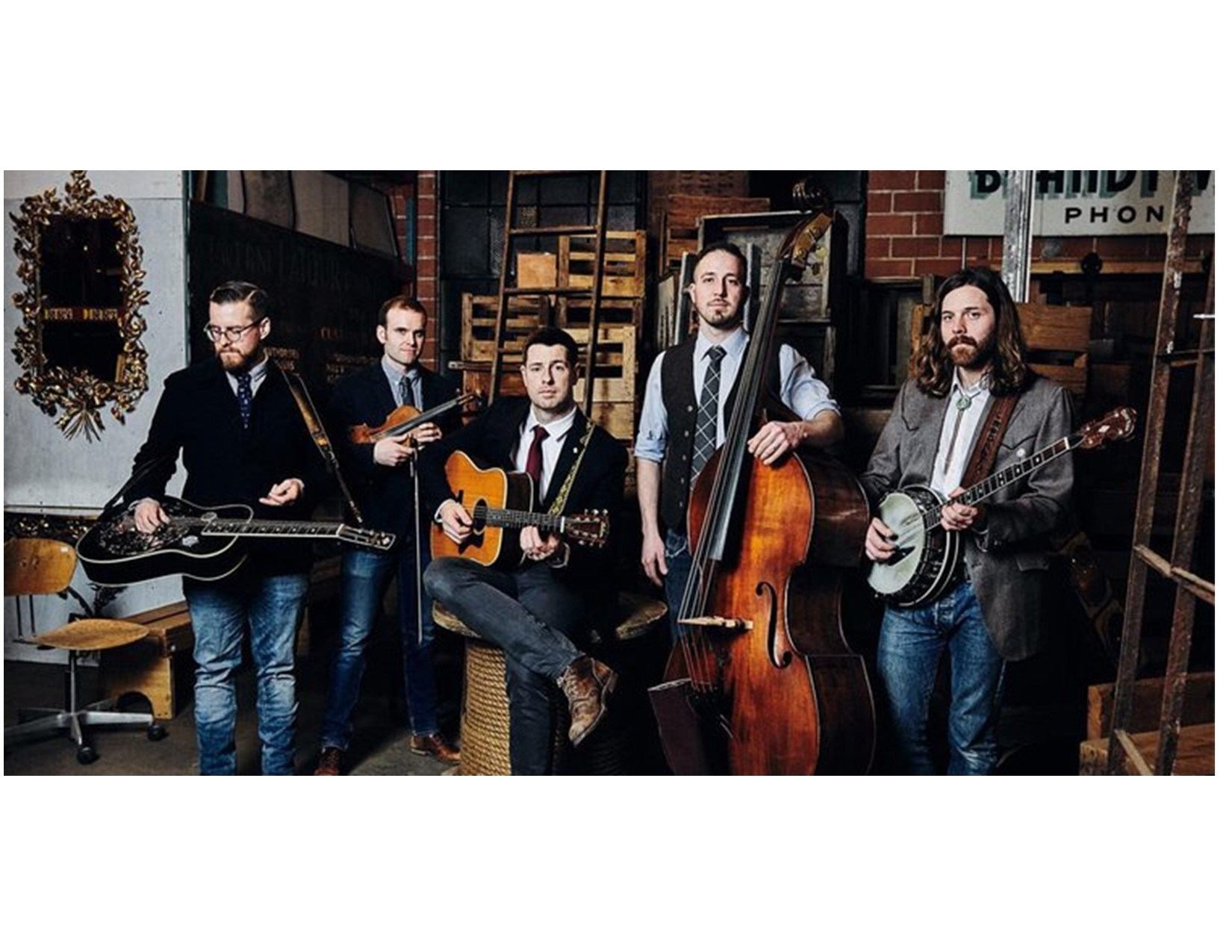 Bluegrass band members perform with guitars and upright bass at a brick venue stage.