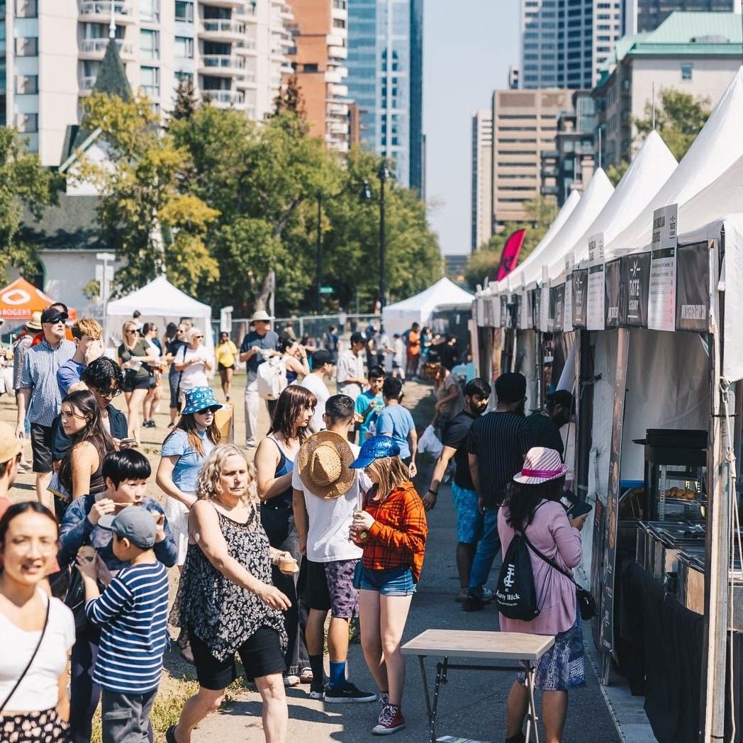 People line up at white vendor tents beside Calgary high-rises.