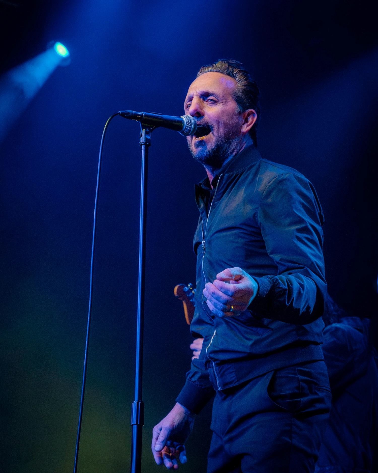 Singer performs into a microphone onstage under blue concert lighting.