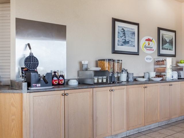 Breakfast counter with waffle maker, cereal dispensers, condiments, and framed wall art.