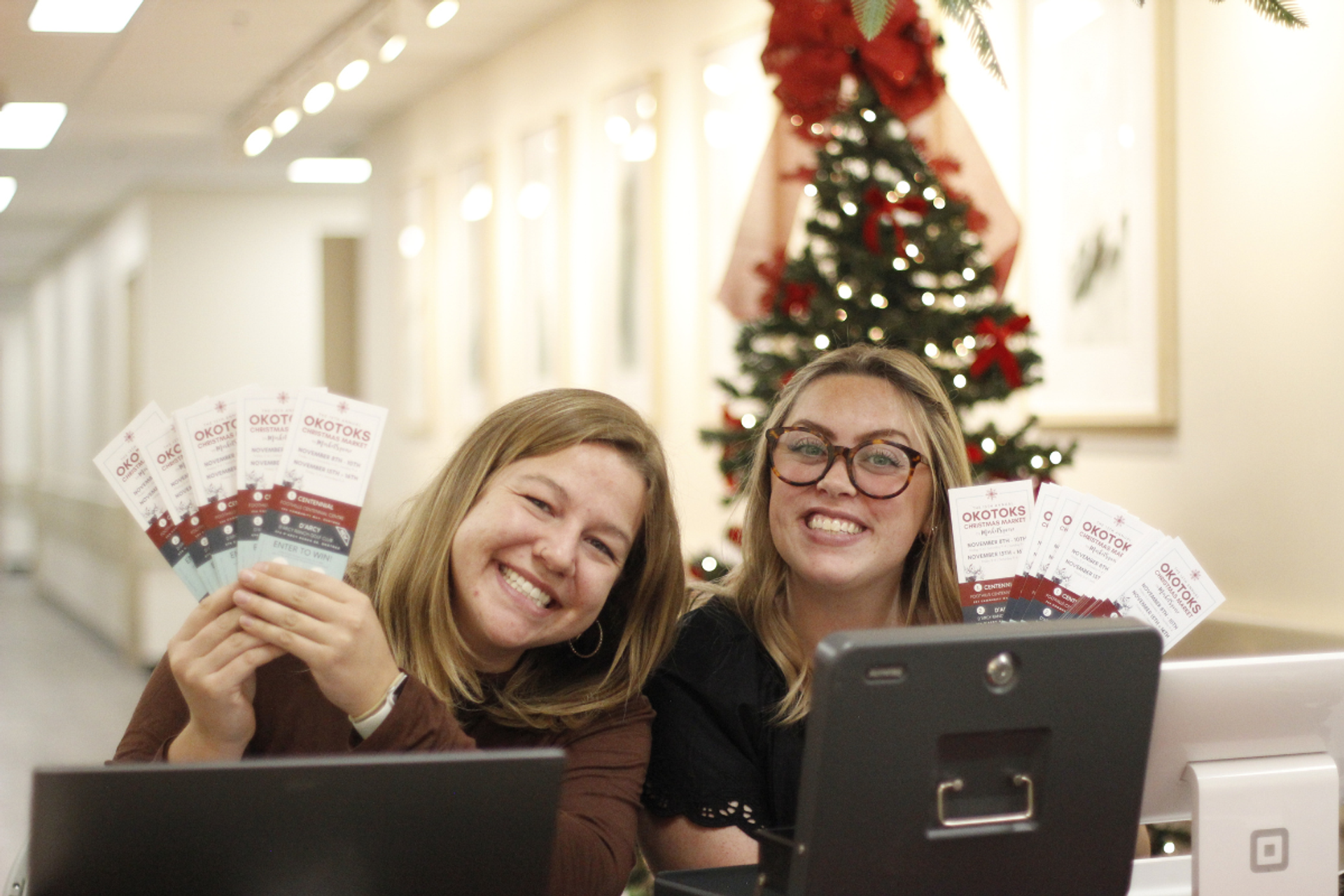 Two people holding tickets at a desk with a decorated Christmas tree in the background.