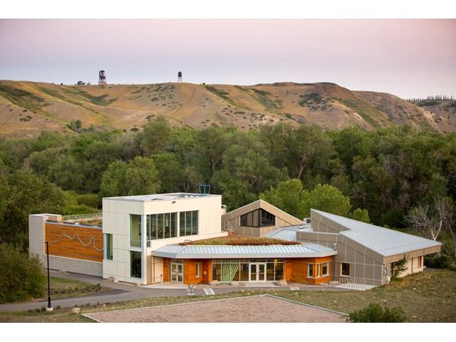 Modern nature centre with tower and sloped roofs, set in lush green landscape.