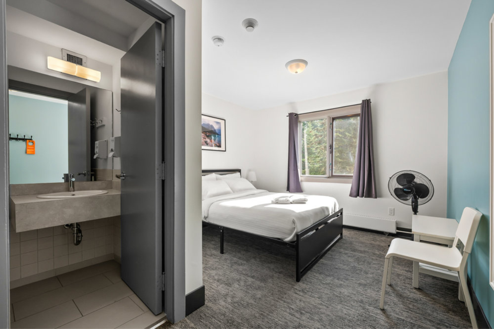 Private ensuite room with queen bed, modern bathroom, chair, natural light from window.