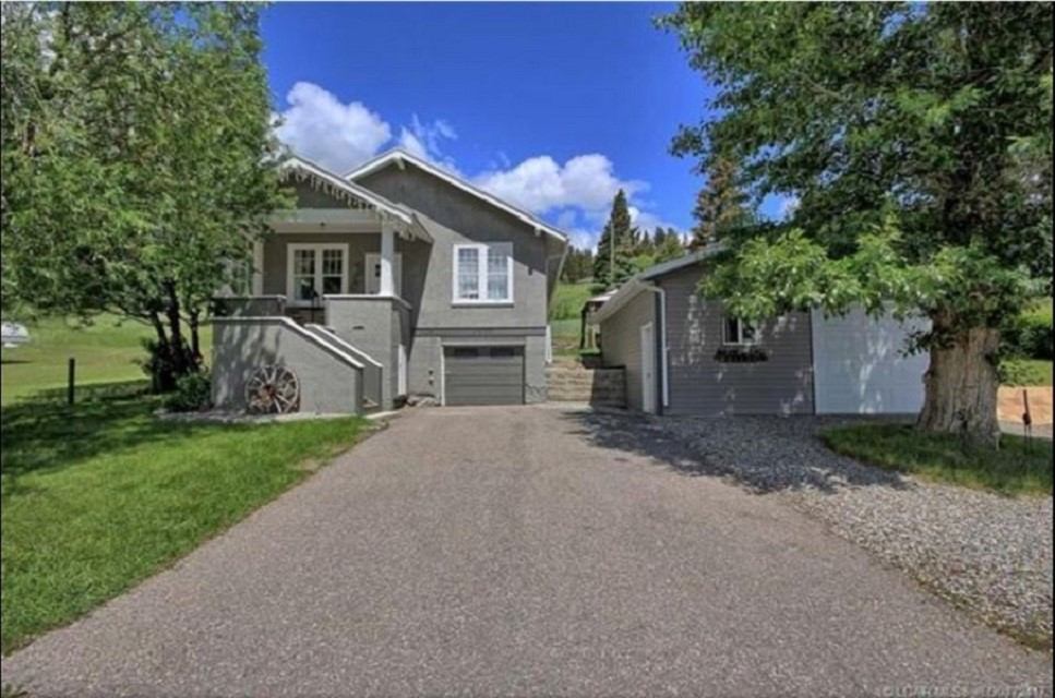 Gray house with garage and driveway surrounded by green trees under blue sky.