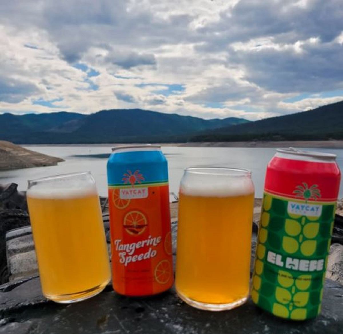 Brewed beer cans and two glasses with mountains and lake in the background.