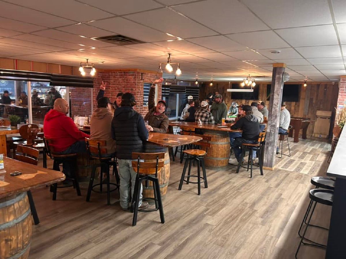 People seated at barrel-style tables inside a rustic brewery taproom.