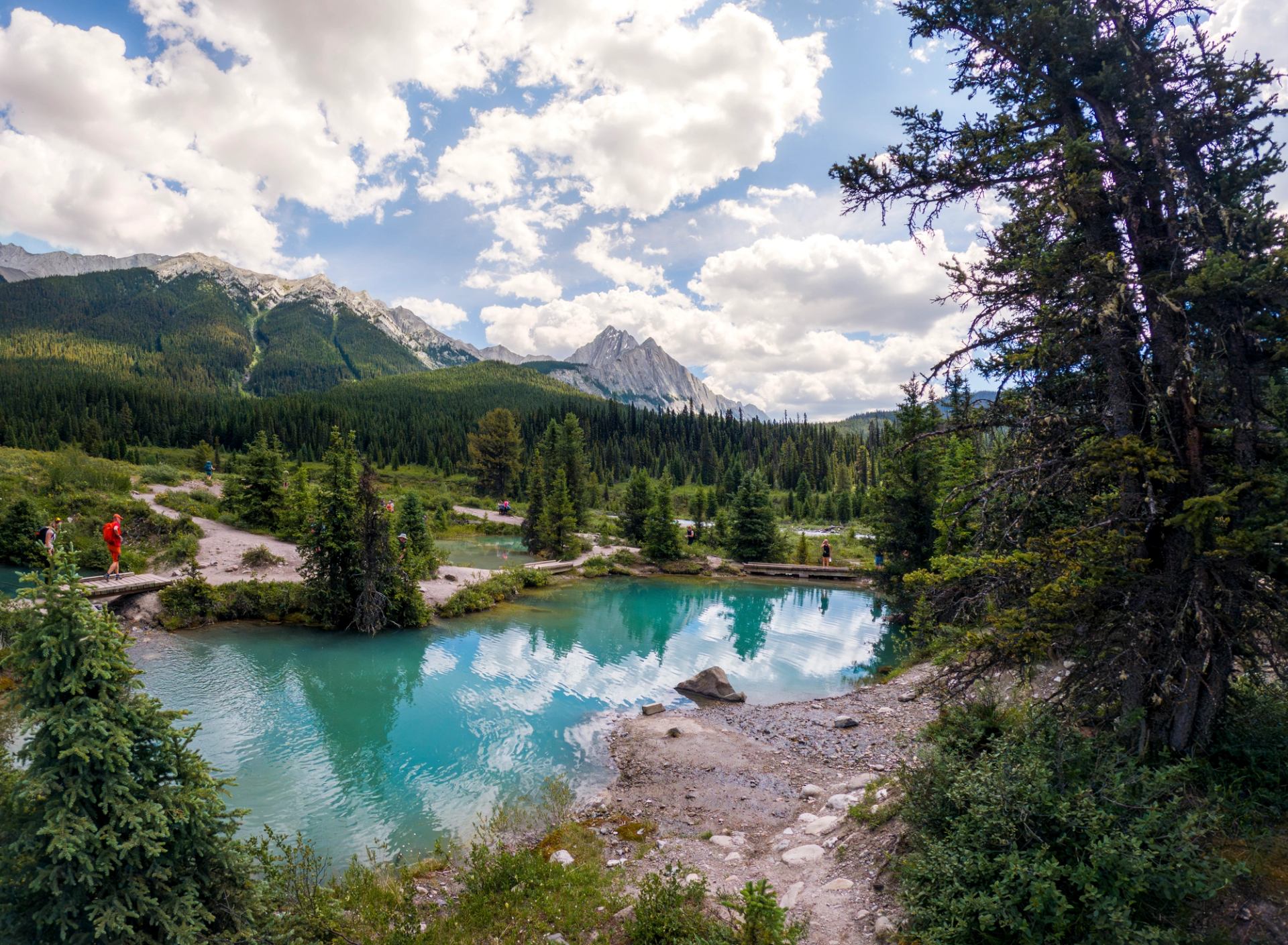 Turquoise ponds sit among evergreen forest and mountain peaks along a hiking trail.