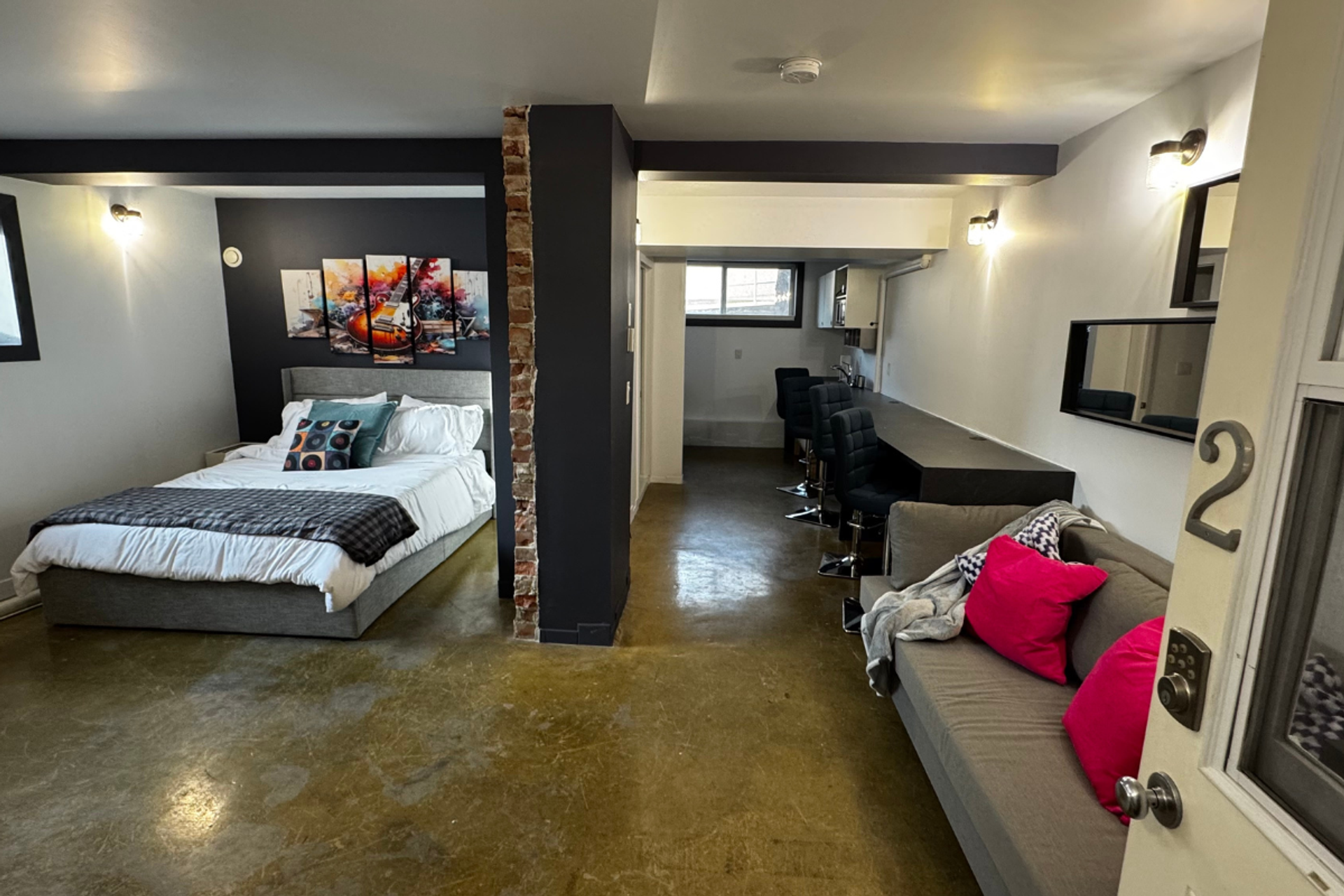 Studio room with bed, sofa, bar counter and guitar artwork on dark accent wall.