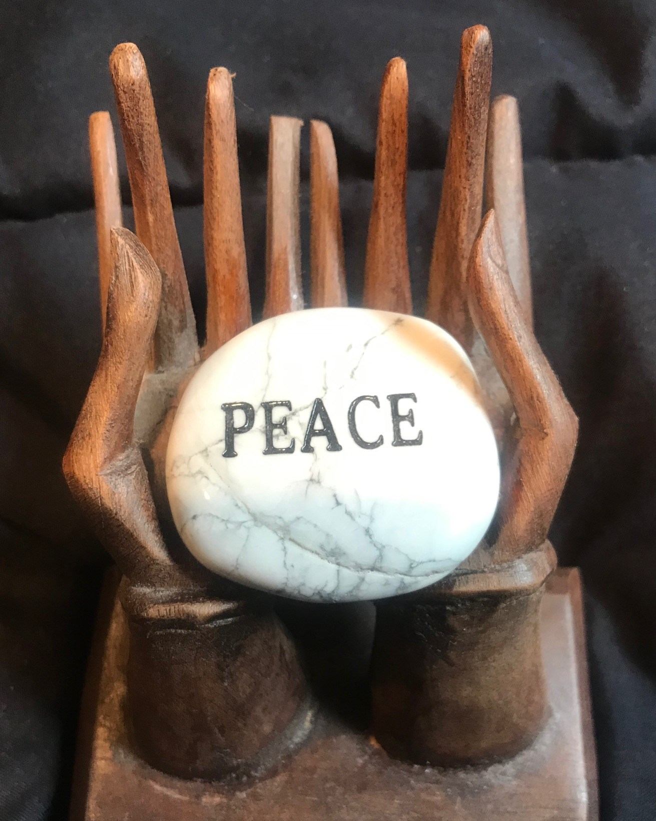 Wooden hand statue holding a peace sphere with the word “PEACE” on it.