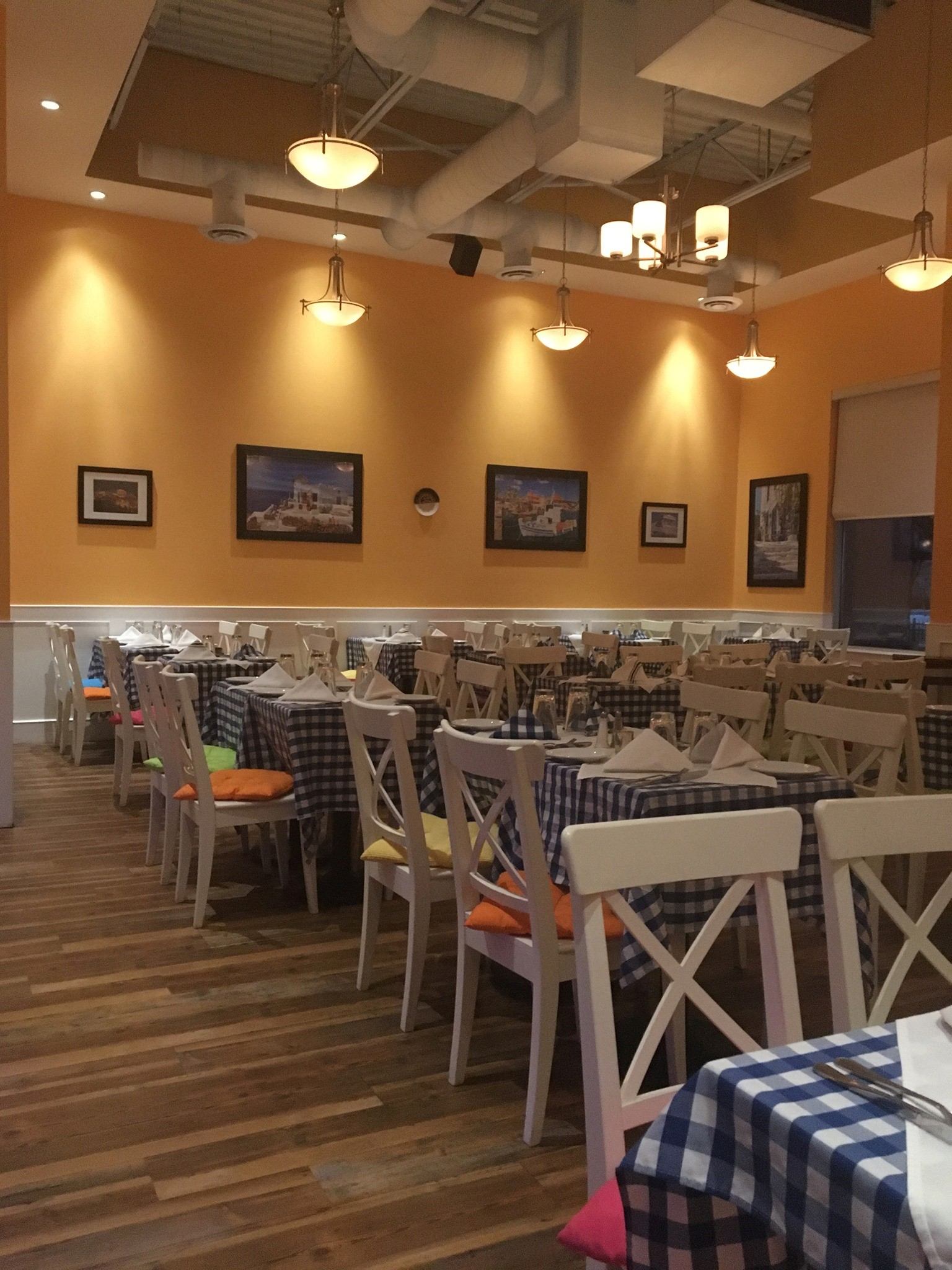 Greek taverna with checkered tables, white chairs, orange walls, and warm lighting.