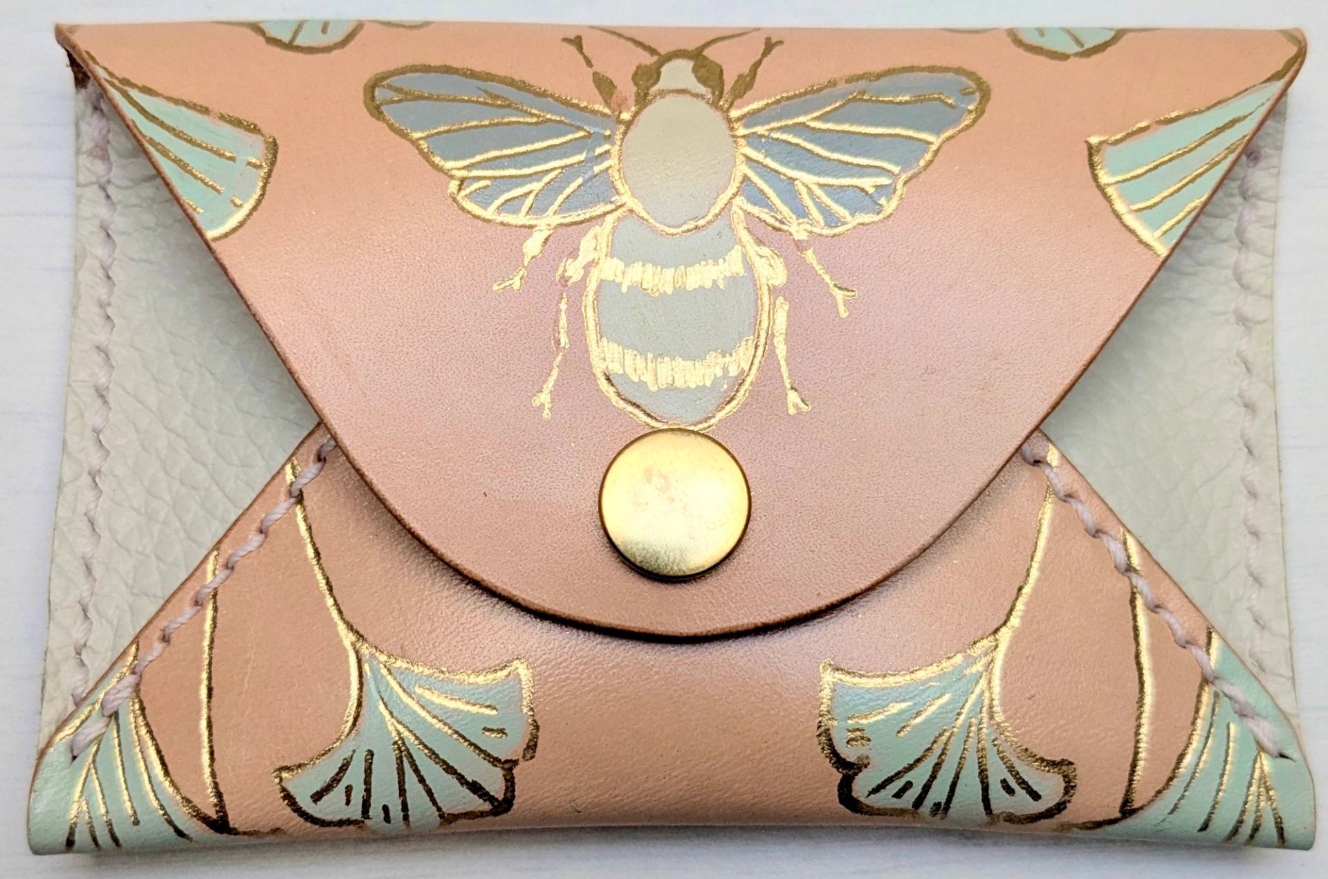 Leather coin purse with gold bee illustration and floral designs on pale pink flap.
