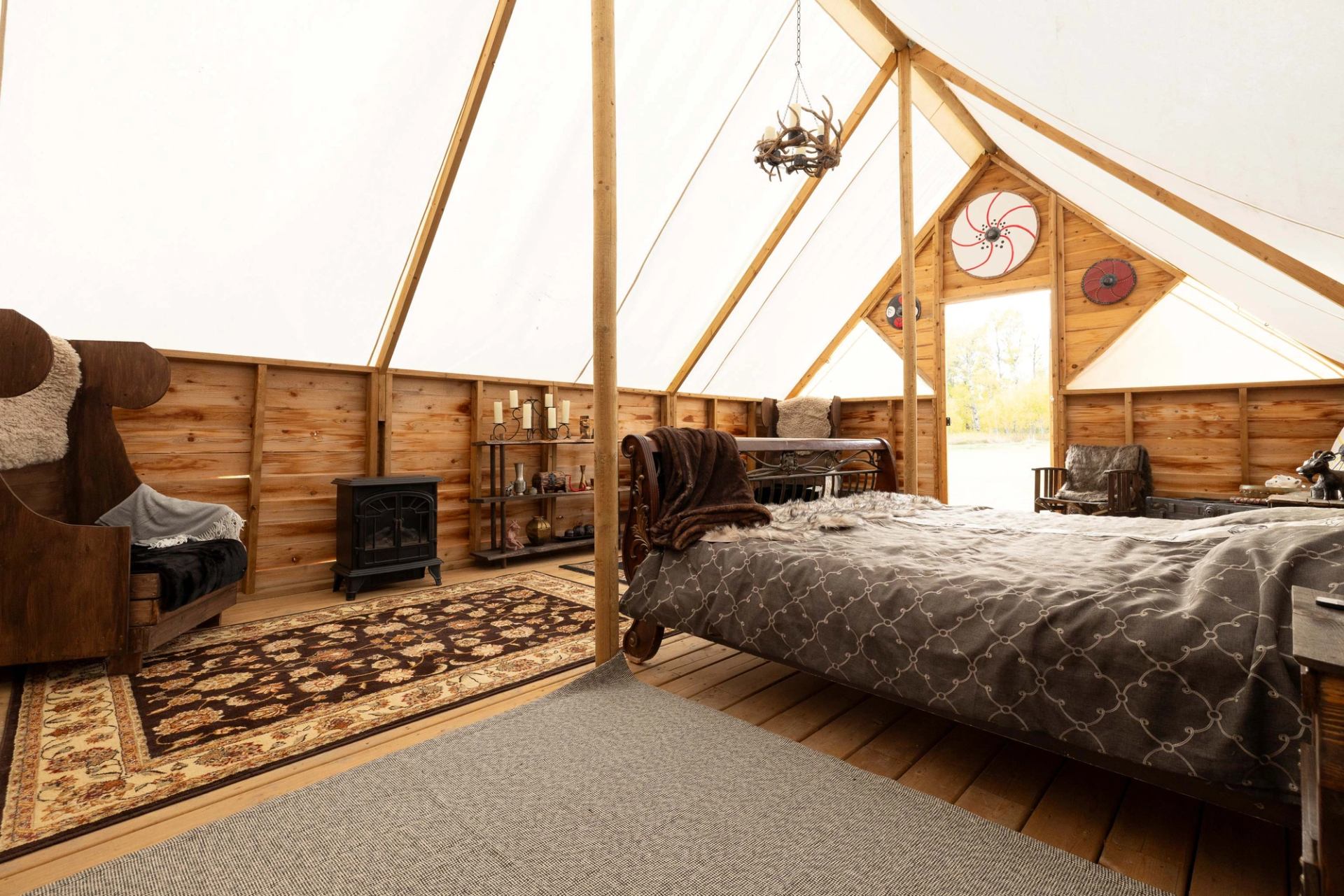 A cozy glamping tent bedroom with a large bed, wood stove, and Viking-themed decor.