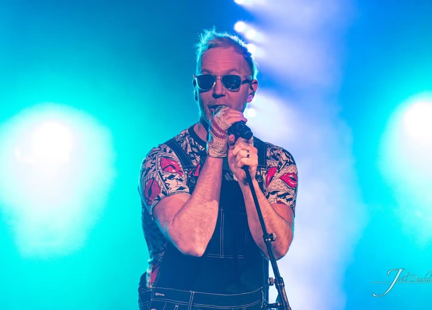 Performer singing on stage with bright lights and colorful outfit.