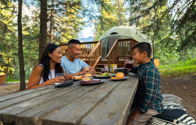 A family sits together for dinner at a picnic table outside of the Glamping Domes at Castle Provincial Park.