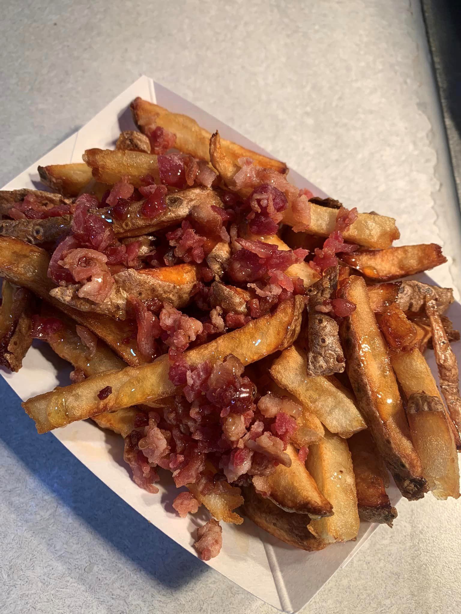 Pile of fries topped with diced meat and chopped pickles on a paper tray.