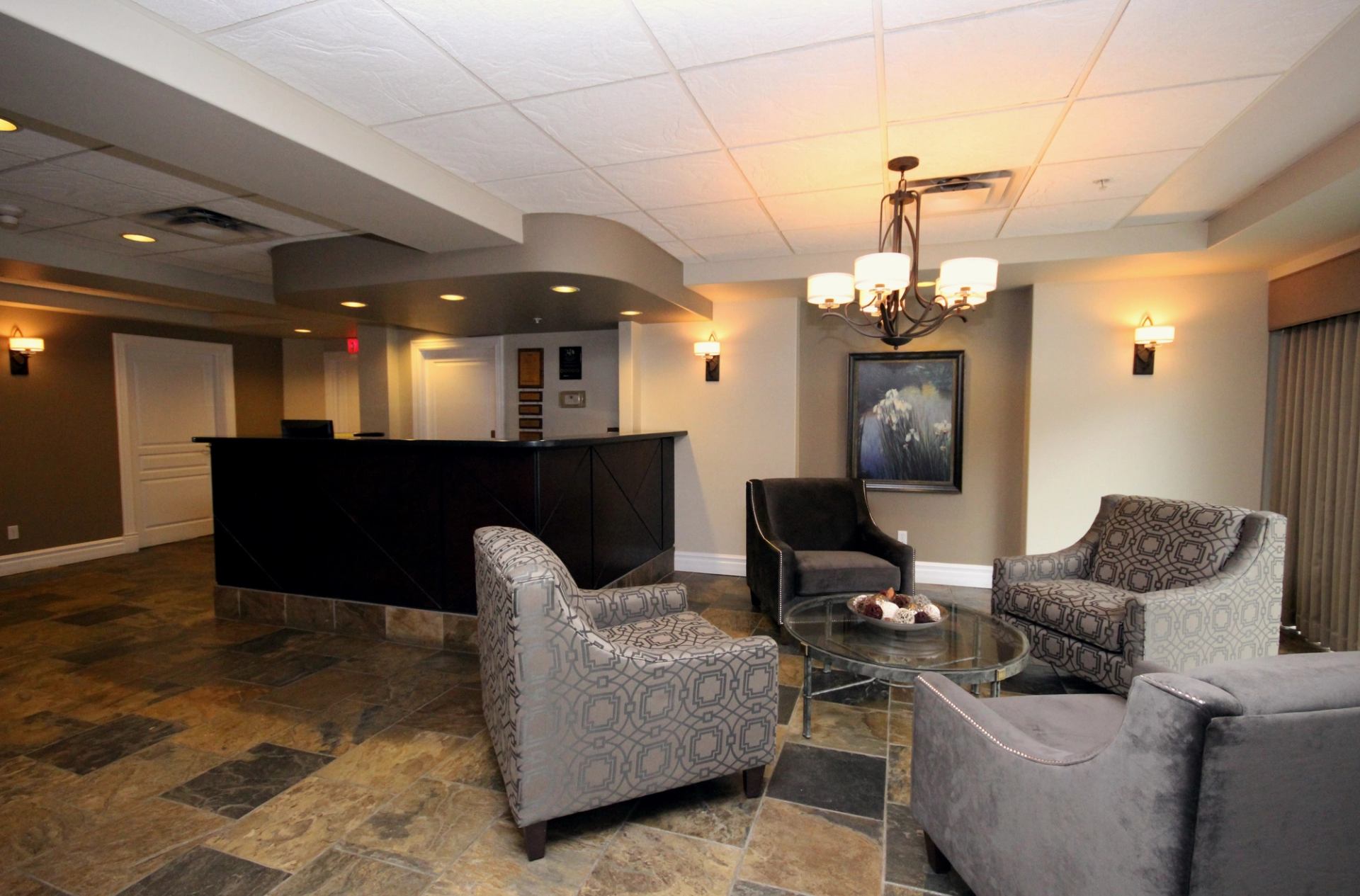 Hotel lobby with stylish chairs, glass coffee table, and front desk in a warm, neutral setting.