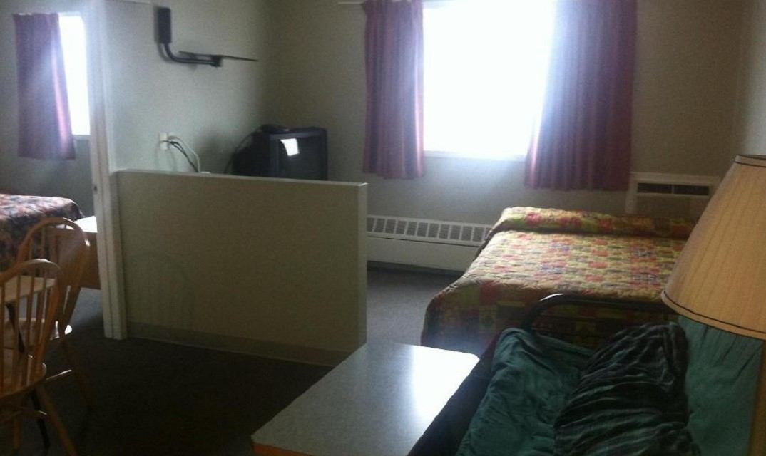 Motel room with two beds, dining table, and TV near a bright window.