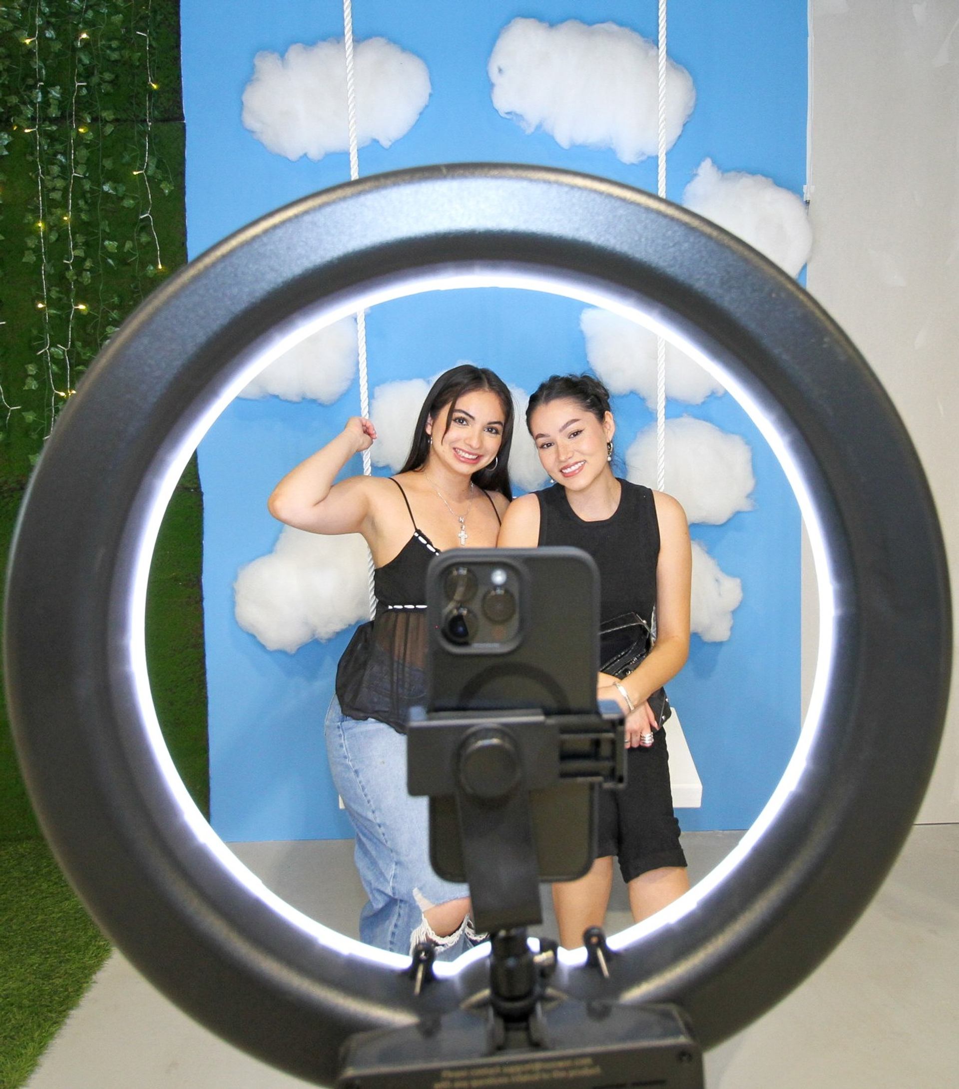 Two people pose on a swing set backdrop, framed by a ring light and smartphone.