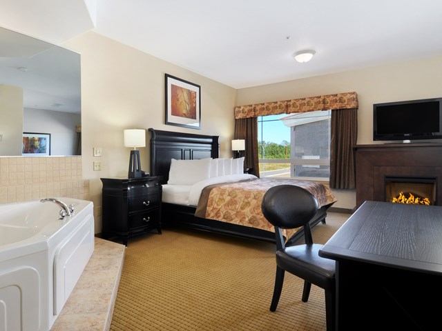 Hotel room with fireplace, desk, large bed, and elevated bathtub.