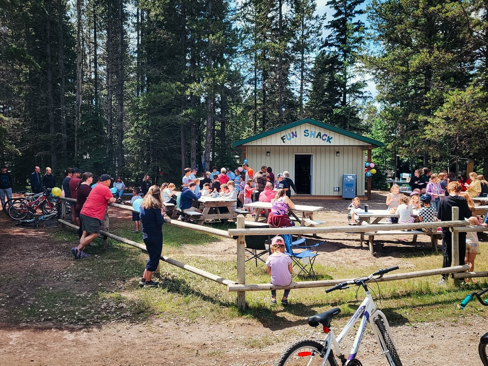 Outdoor gathering at Fun Shack building with people sitting at picnic tables and bicycles nearby.