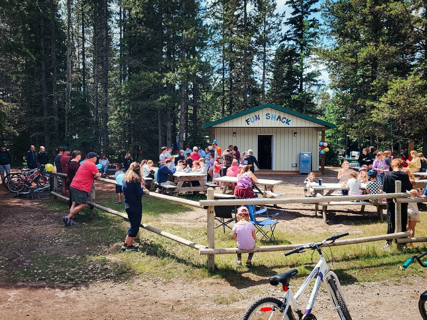 Outdoor gathering at Fun Shack building with people sitting at picnic tables and bicycles nearby.