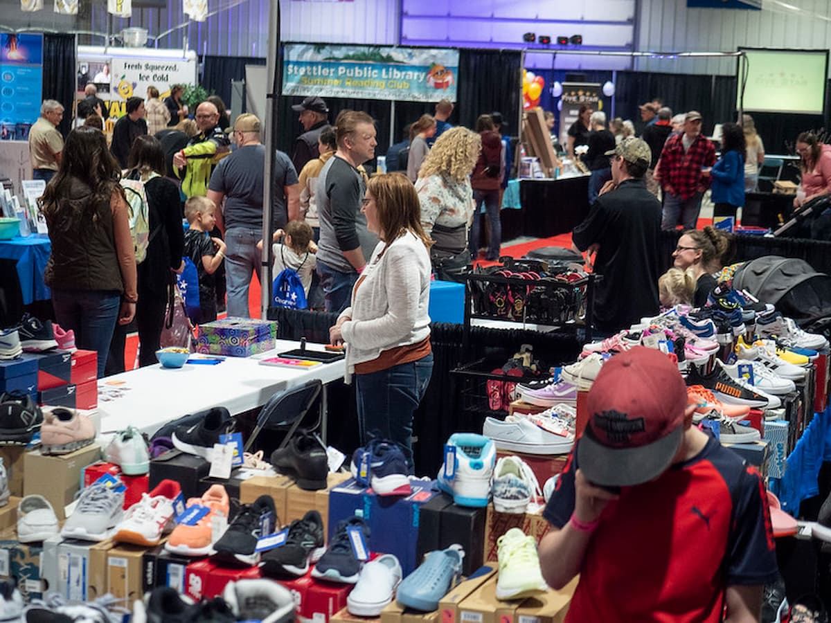 Crowds browse tables of shoes and goods at indoor trade show.