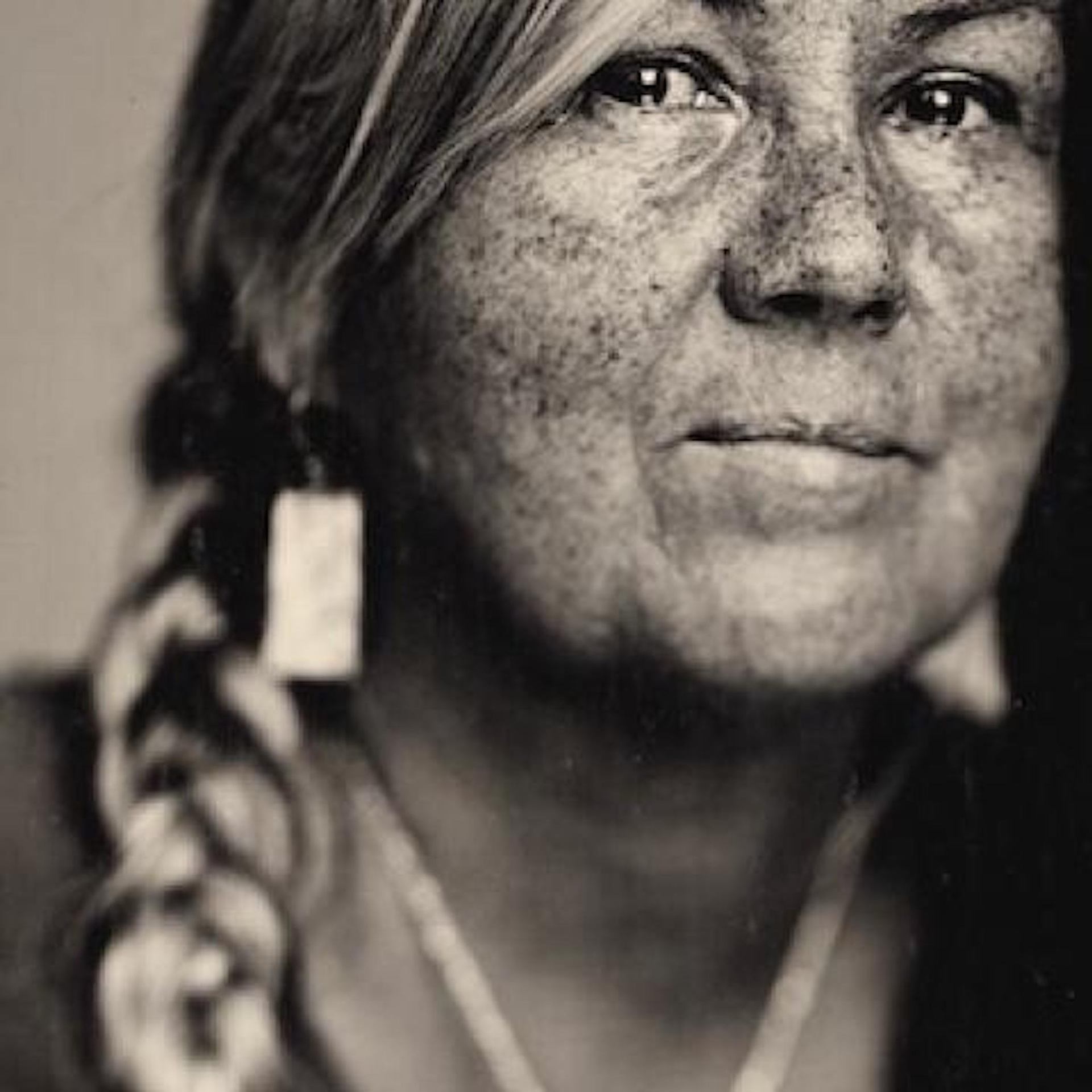 Close-up of a braid with a square earring and necklace, captured in a sepia-toned artistic style.