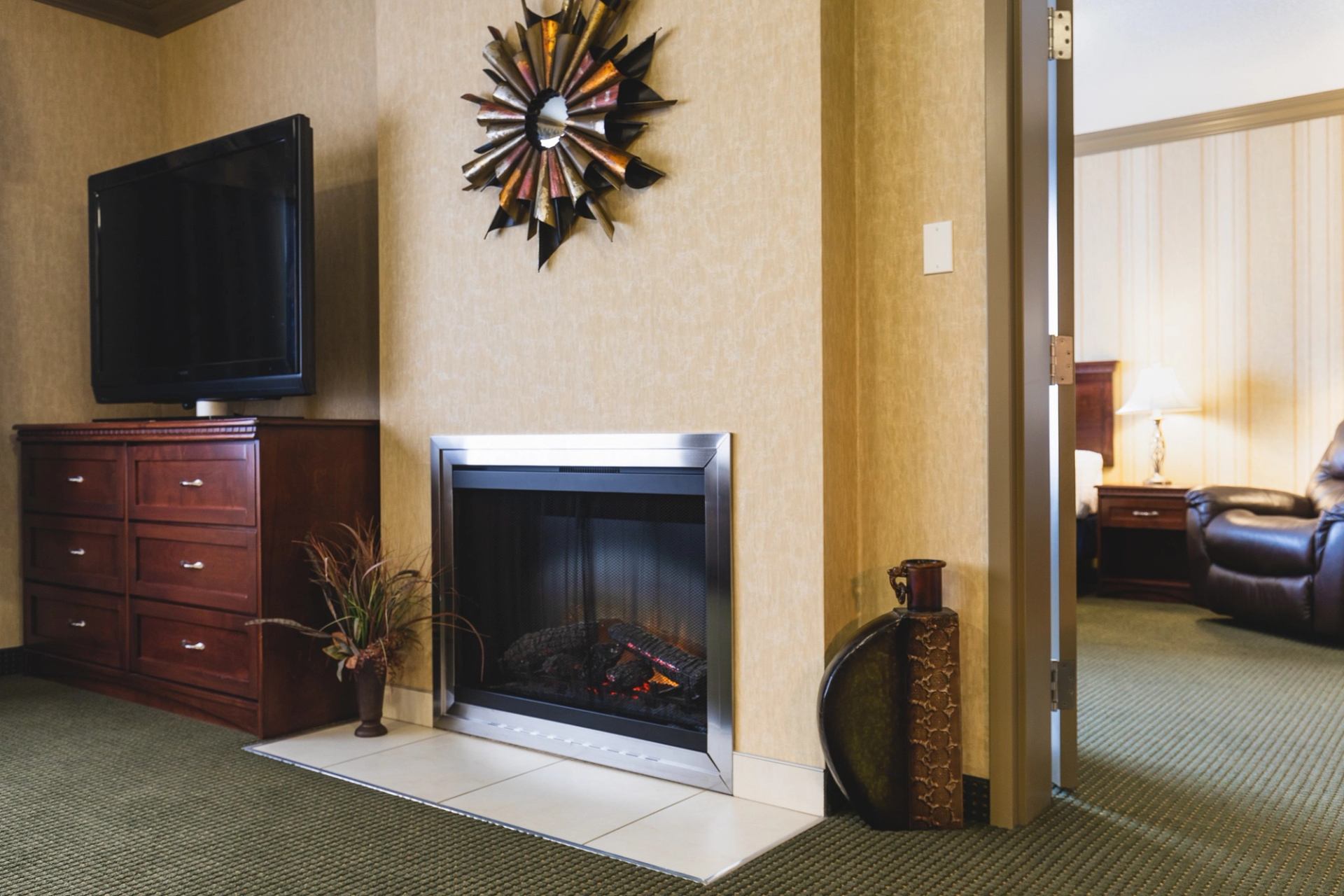 Hotel room fireplace, TV, dresser, decorative wall clock, and lamp in doorway view.