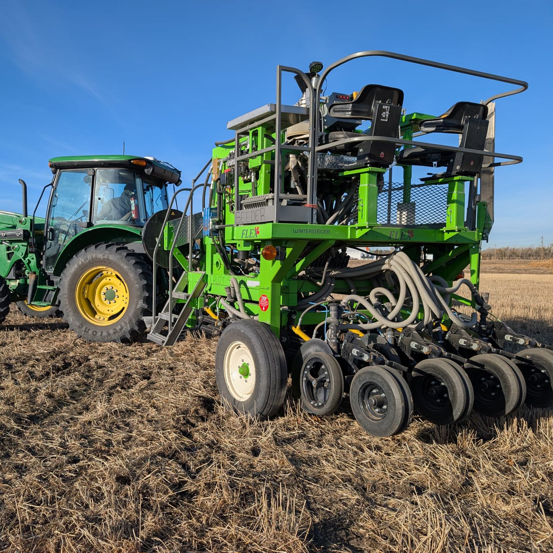 Green tractor towing large green seeding machine across dry harvested farm field.
