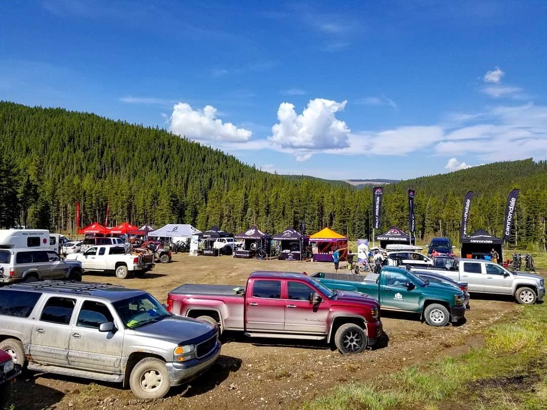 Trucks and tents gathered in a forest clearing under a blue sky with hills in the background.