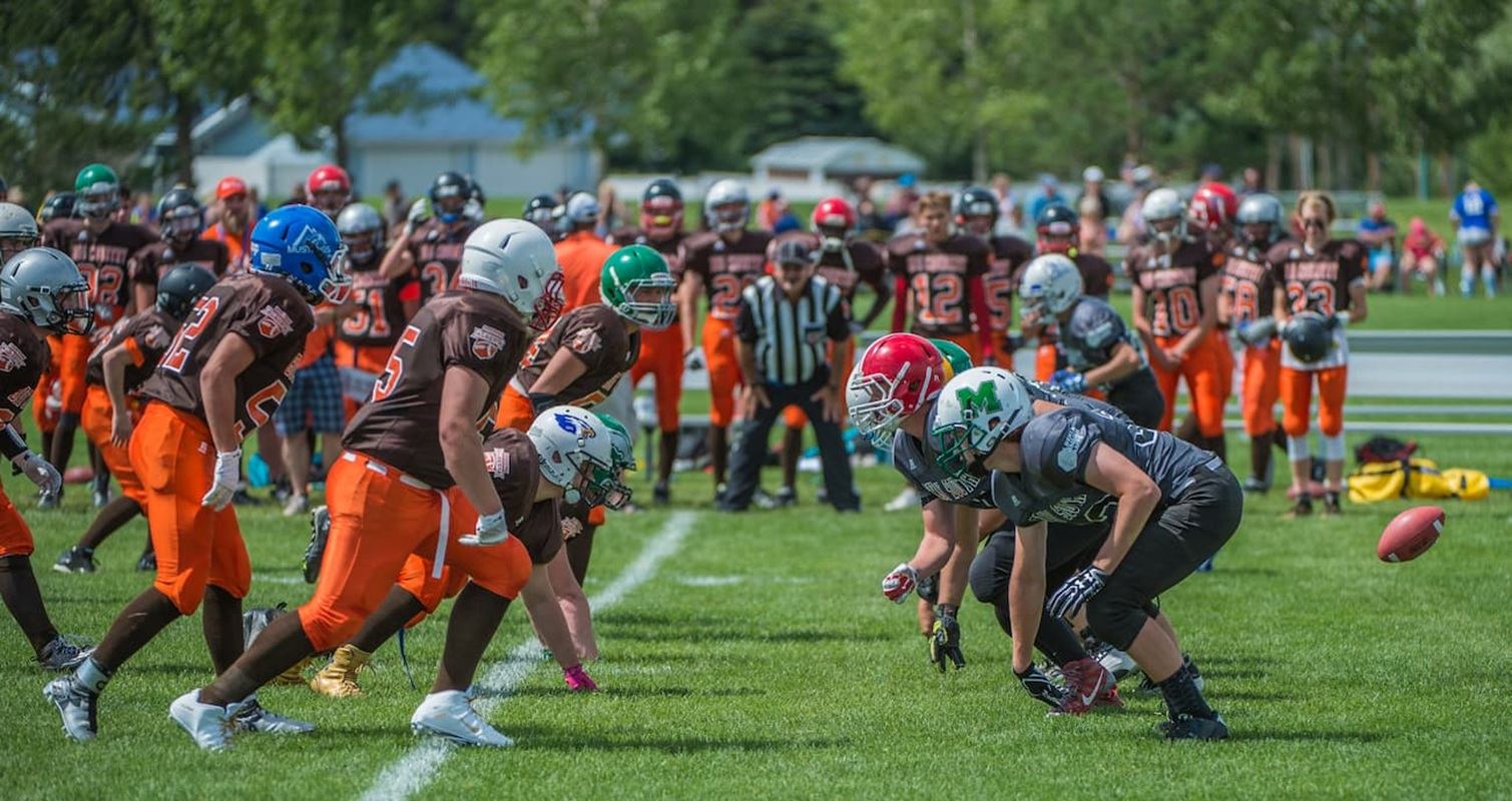 Youth football teams line up at scrimmage as ball is snapped on grassy field.