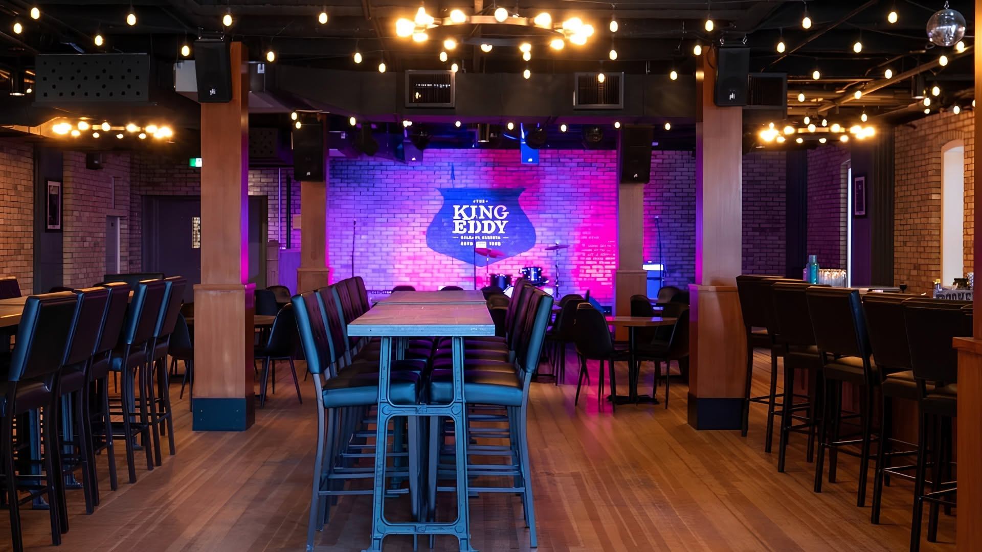 Restaurant stage with King Eddy sign, bar tables, chairs and hanging string lights.