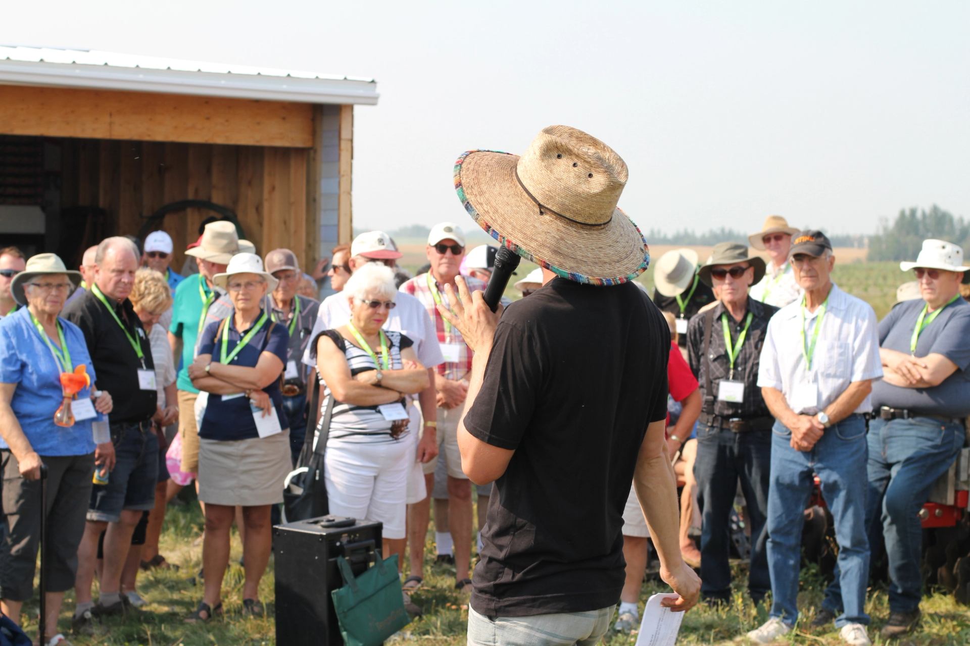 A group gathered outdoors listening to a speaker during a farm tour.
