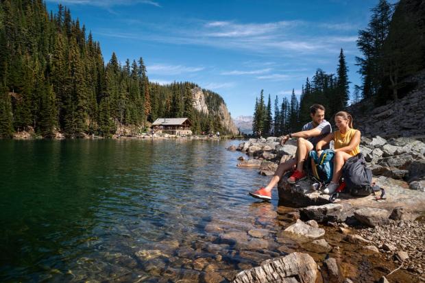 People sit on the water's edge after hiking to Lake Agnes Tea House in Banff National Park.