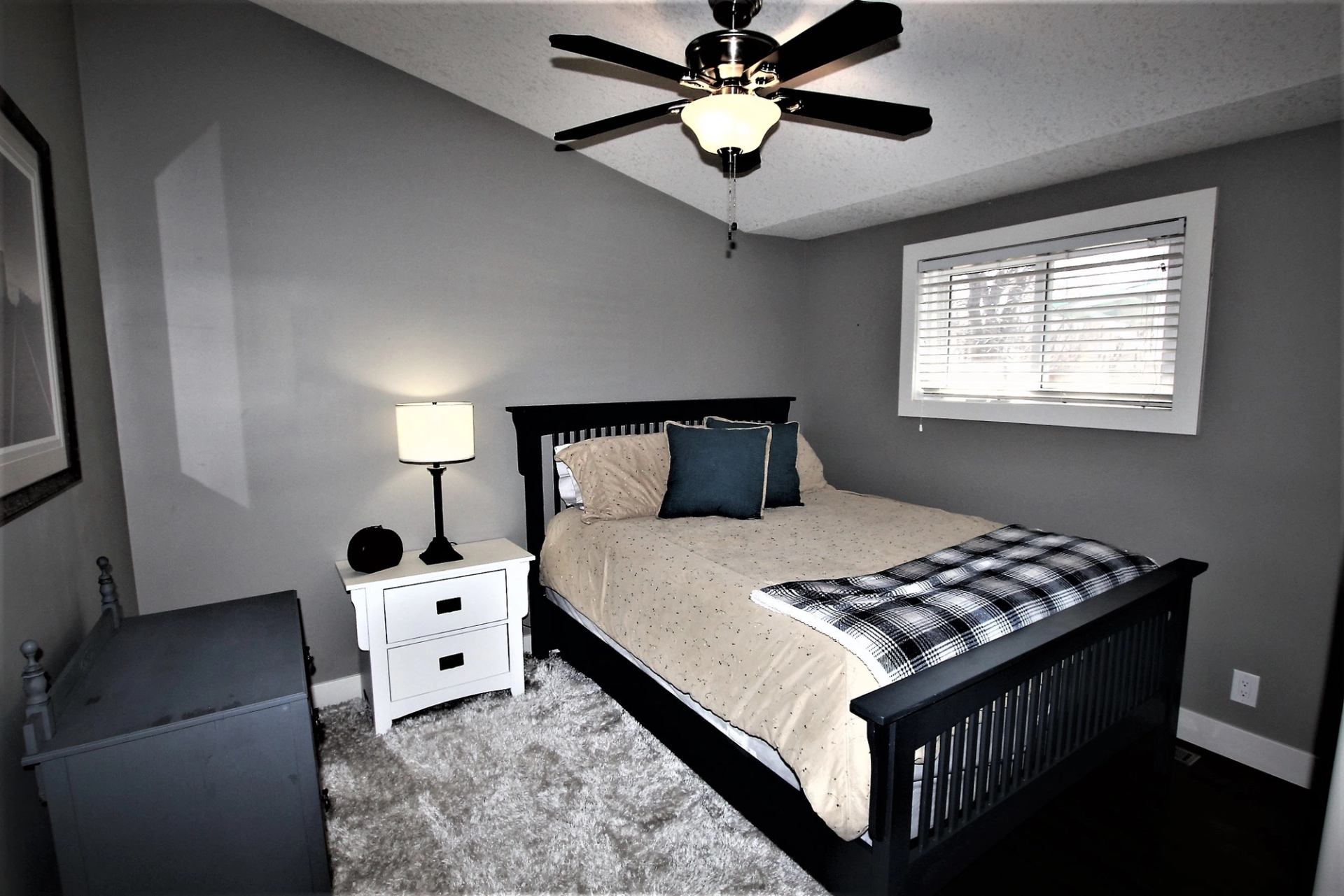 Cozy bedroom with dark wood bed, ceiling fan, and soft carpet flooring.
