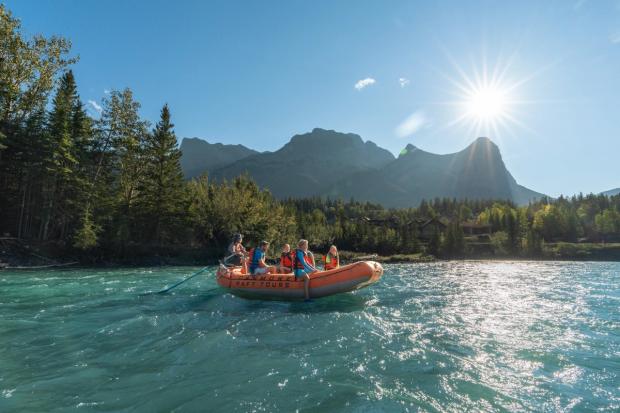 A family floats down the Bow River with Canmore Raft Tours as the sun flares over top of the mountains in Canmore.