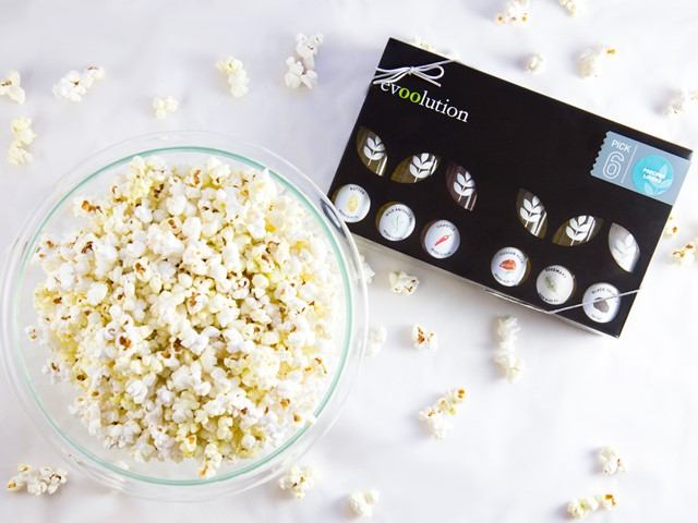 Glass bowl of white popcorn beside evoolution product box with poppyseed designs and stickers.