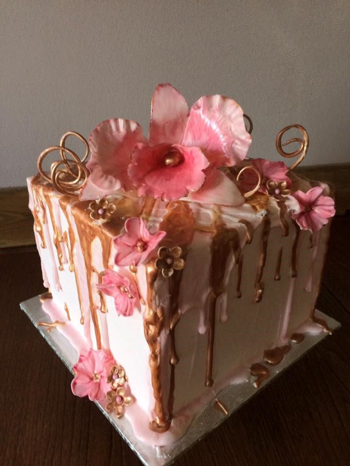 Decorated pink and gold cake with flower and drip icing on a square tray.