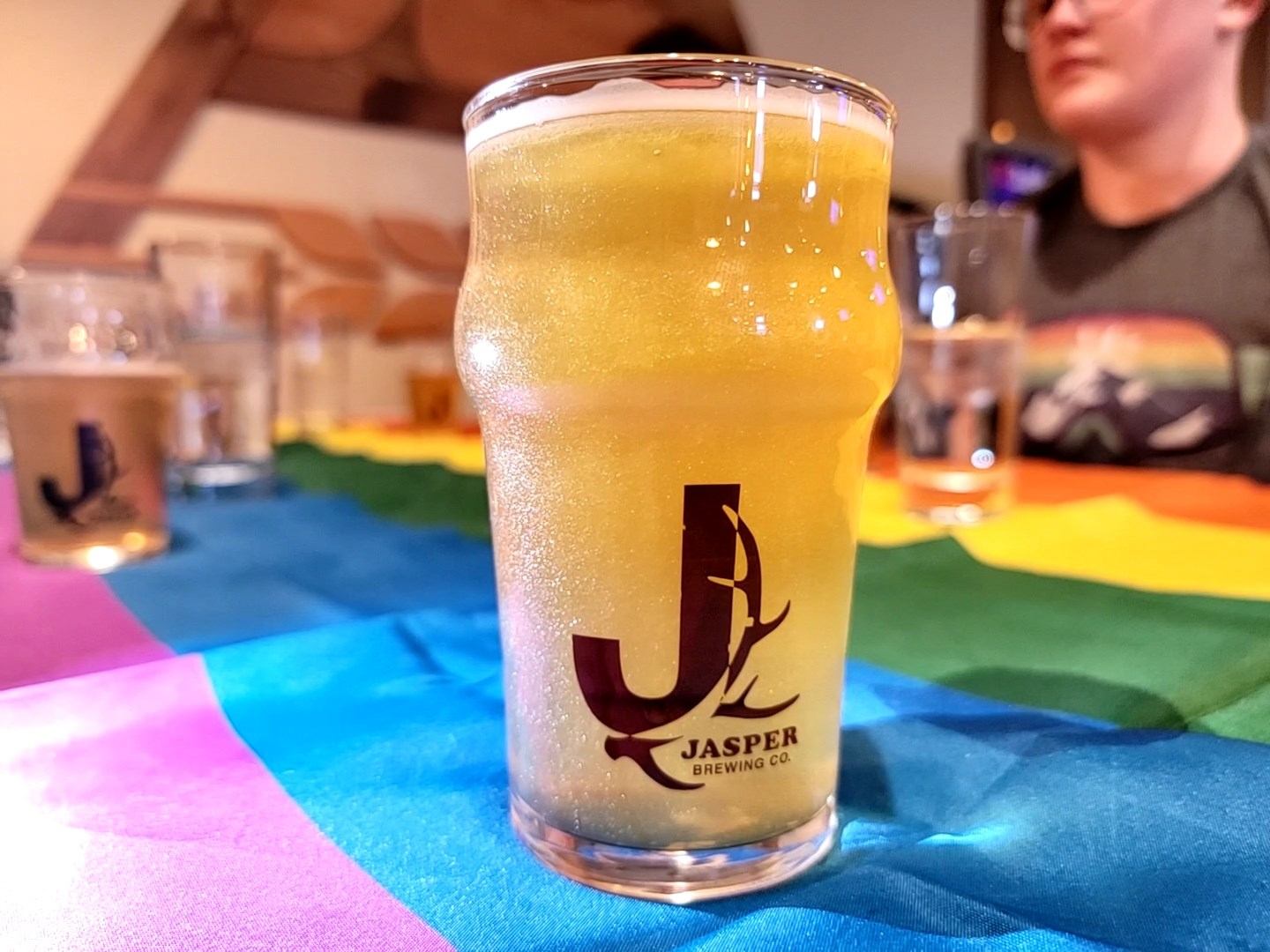 A pint of beer on a rainbow flag with people sitting in the background.