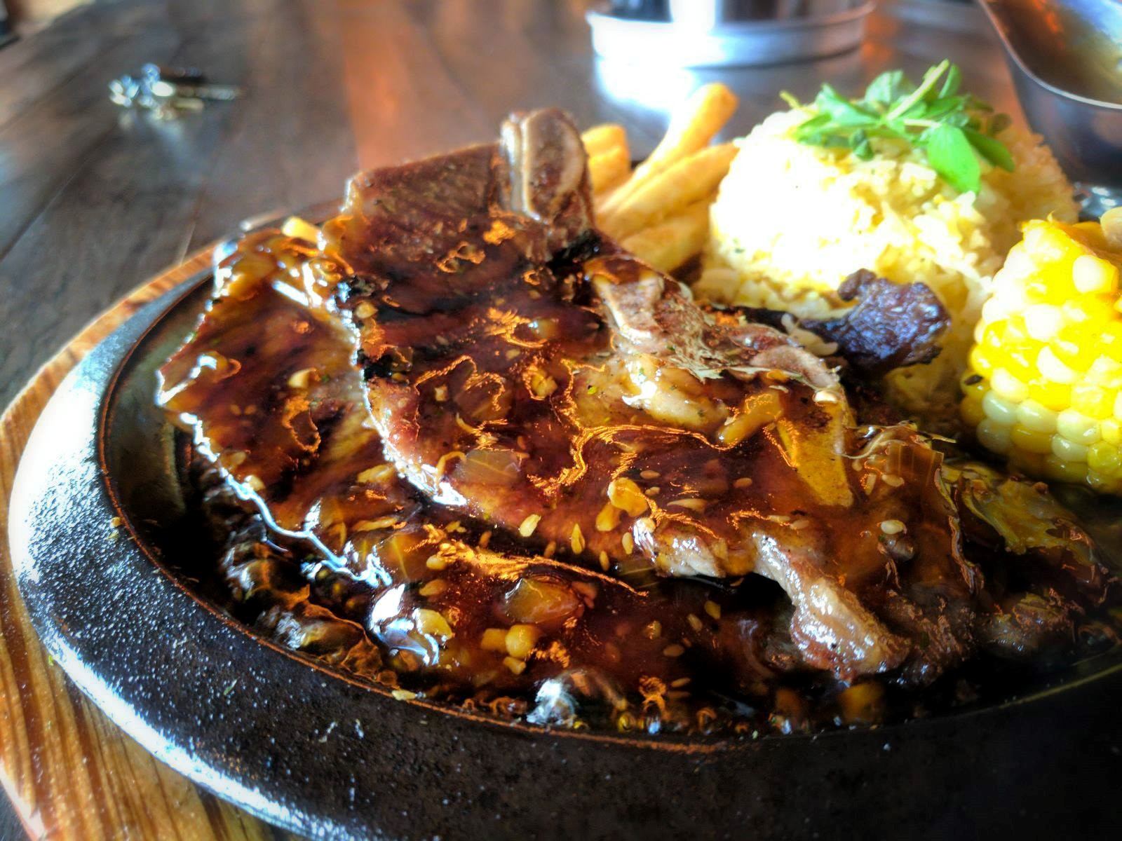 Plated ribs with corn and roasted potatoes garnished with herbs and sauce.