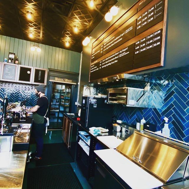 Interior of a brewery with bar taps, chalkboard menu, and customers at the counter.