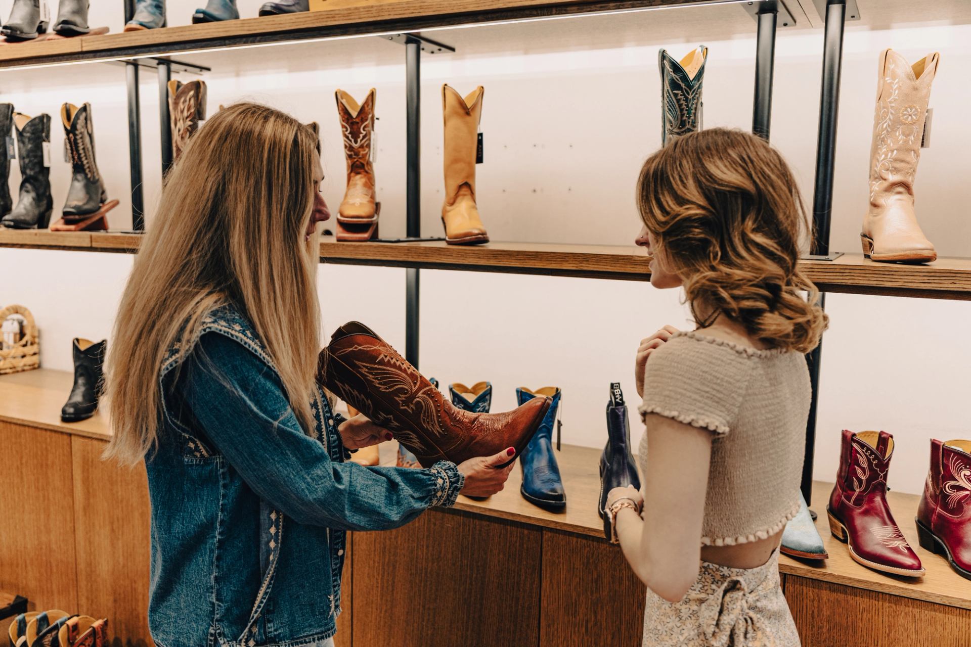 Shoppers examine a brown cowboy boot in a store lined with colourful leather boots.