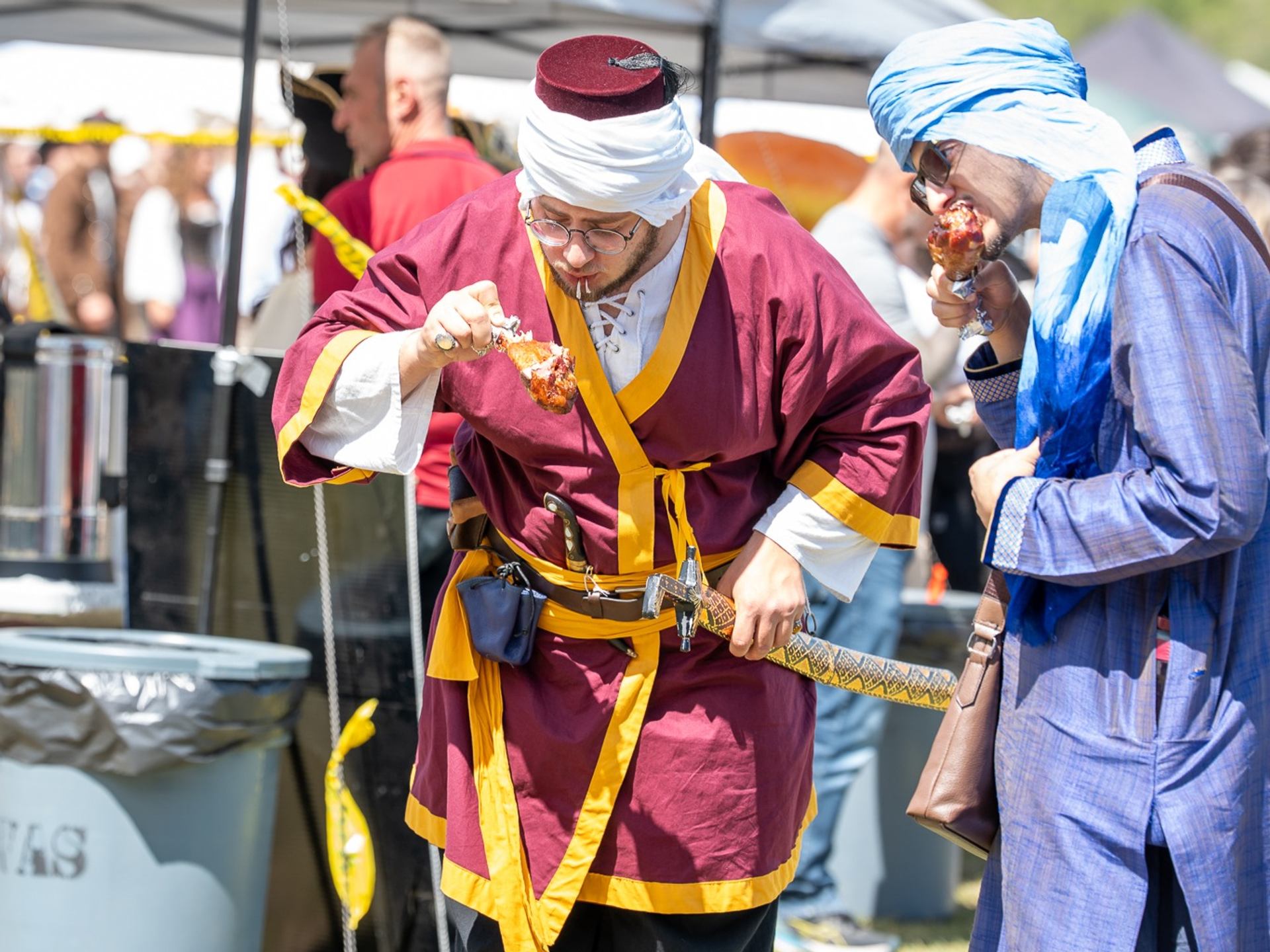 Two people in medieval-style clothing taking part in a live demonstration at an outdoor festival setting.