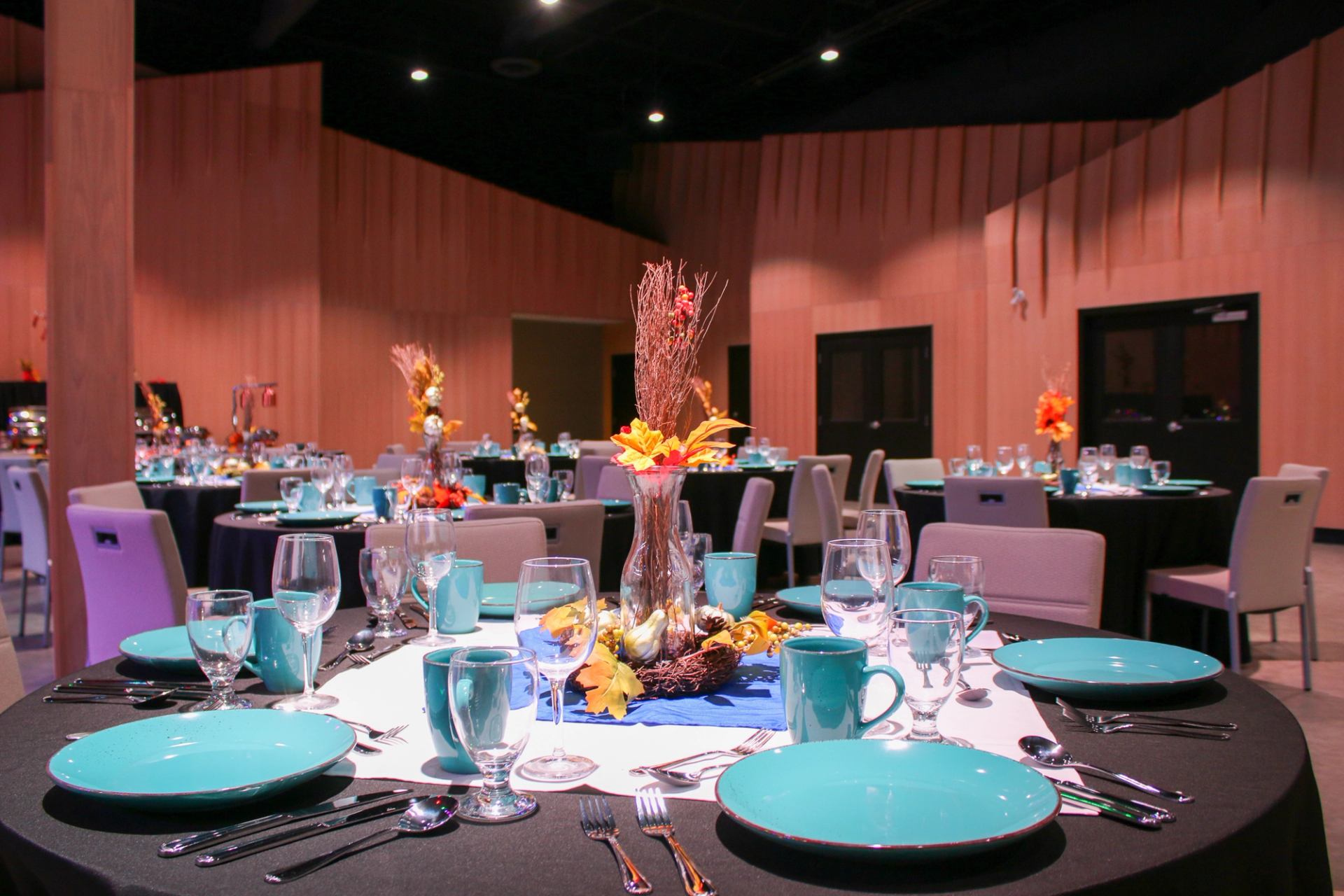 Round tables with black cloths, turquoise plates, and autumn-themed centerpieces.