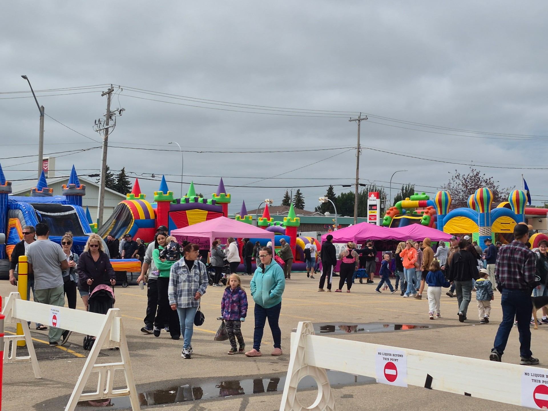 Crowd walking through outdoor fair with colourful inflatable castles and tents in parking lot.