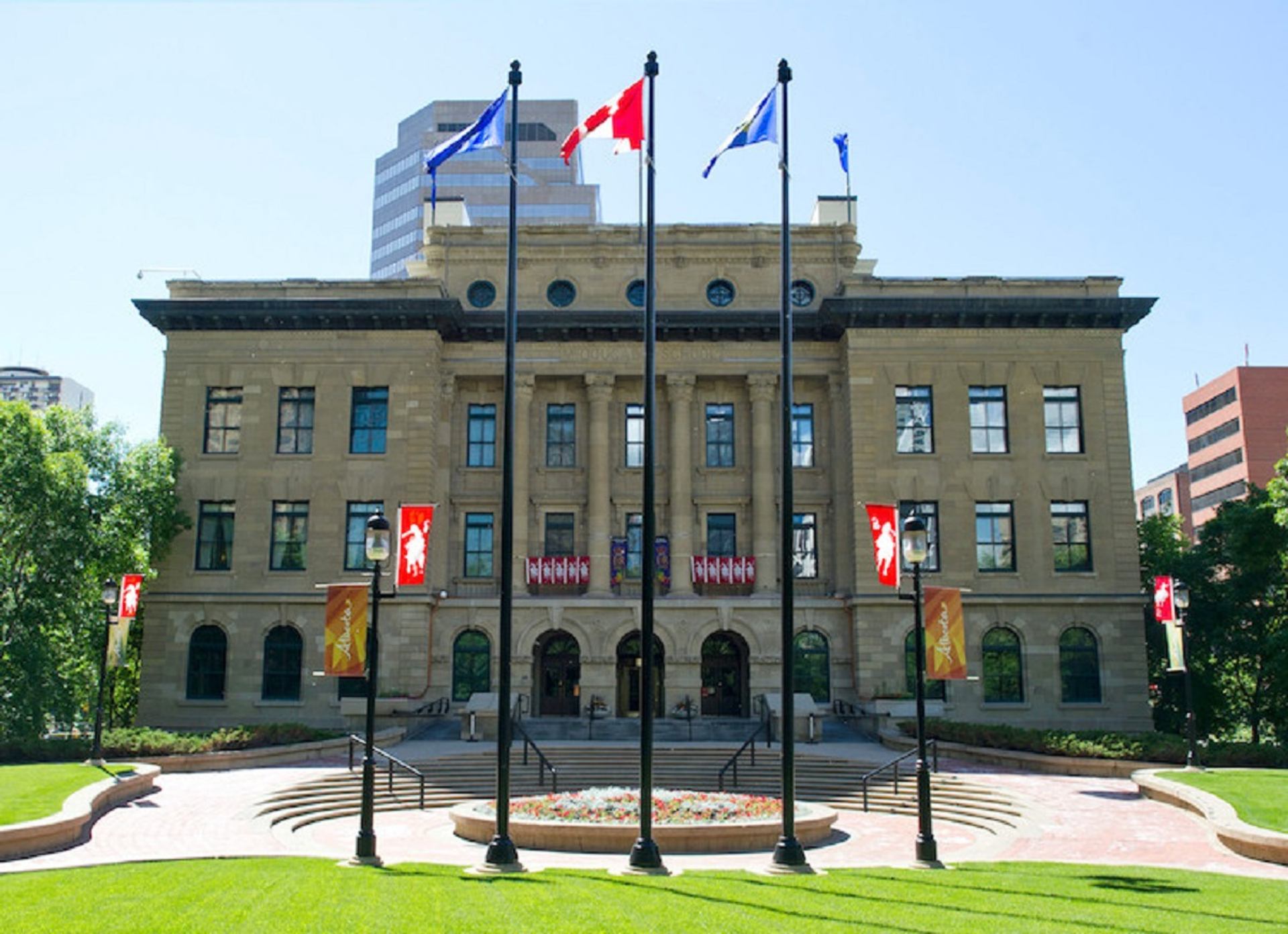 Legislative Building with Canadian and provincial flags flying above a manicured lawn.